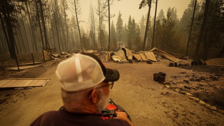 A man looks at the remains of a home as wildfire haze hangs in the air.