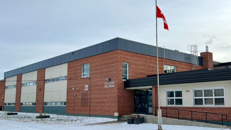 A school is seen from the outside, in winter, with a Canadian flag flying atop a pole.