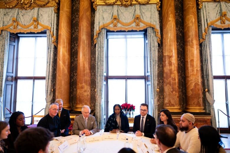 Several people sit at a round table in an elaborately decorated room.