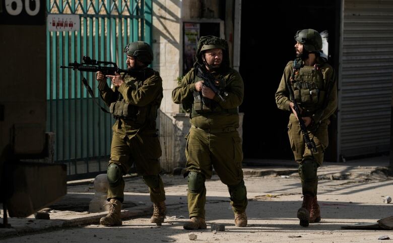 Three soldiers point their guns as they walk down a street.