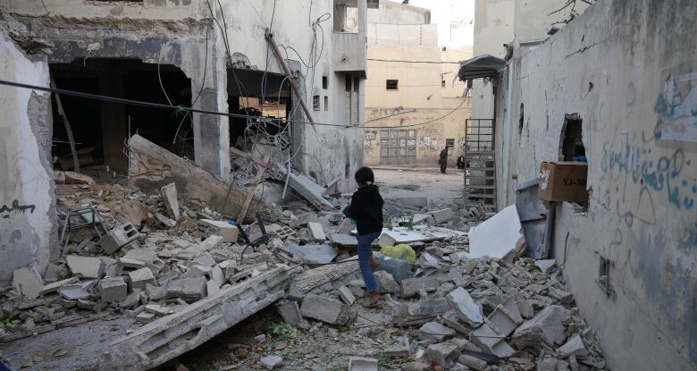 A girl walks among rubble of a destroyed street.