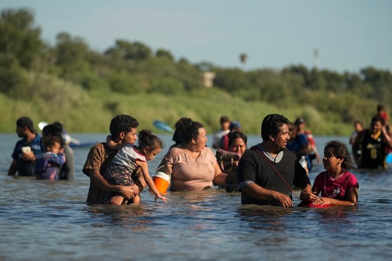 Several people are shown up to their waist or higher in a body of water, wearing clothes.