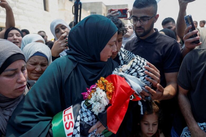 A grieving woman holds the body of a small child with a black and white Palestinian keffiyeh and a red, white, green and black flag draped over him.