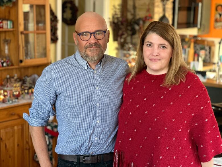 A man in a blue button down shirt and glasses standing next to a woman in a red shirt. 