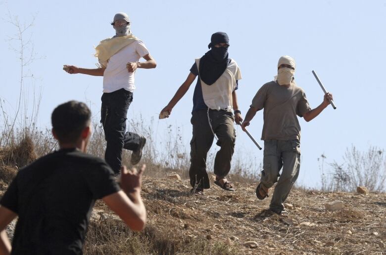 Three masked men advance down a ridge.