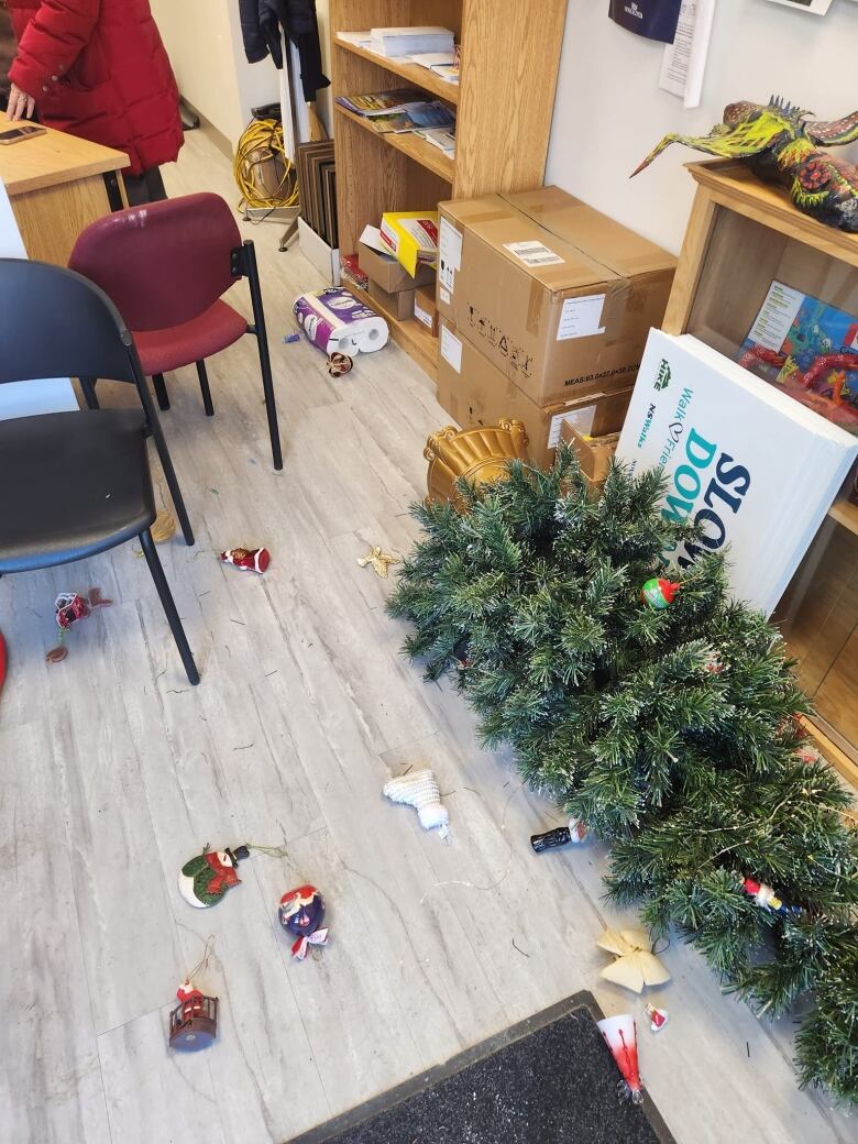 A Christmas tree and ornaments are splayed on the ground inside an office.