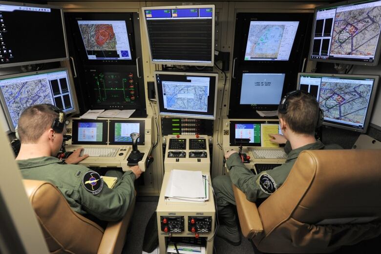 Drone pilots sit in a remote cockpit.