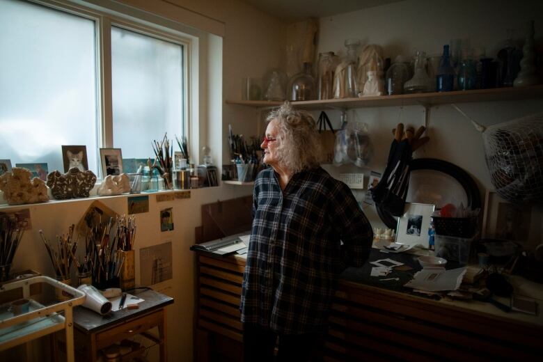 Susanna Blunt leans against an artist's worktable. all around her are paintbrushes, sculptures in progress and artists' tools.