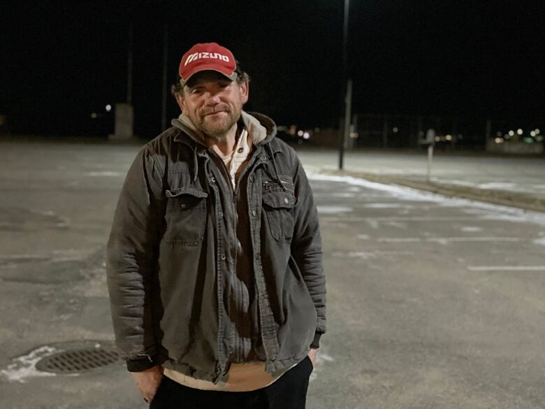 Man standing in parking lot wearing ball hat.