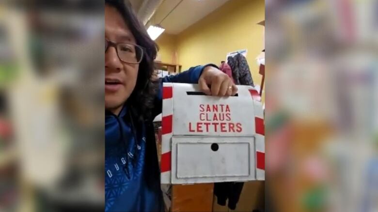 A man holds up a 'Santa Claus Letters' mailbox.