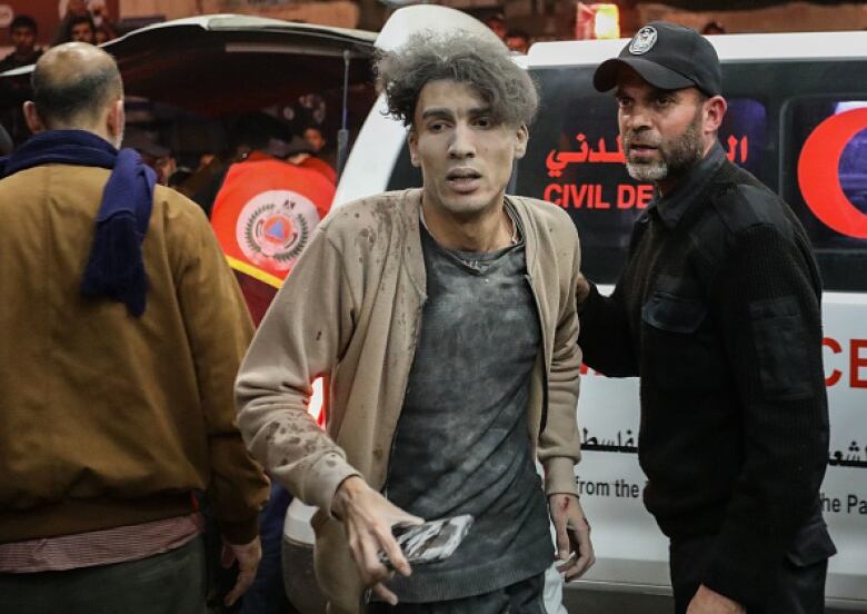 A young man, his face and hair covered in dust, is helped by medical professionals.