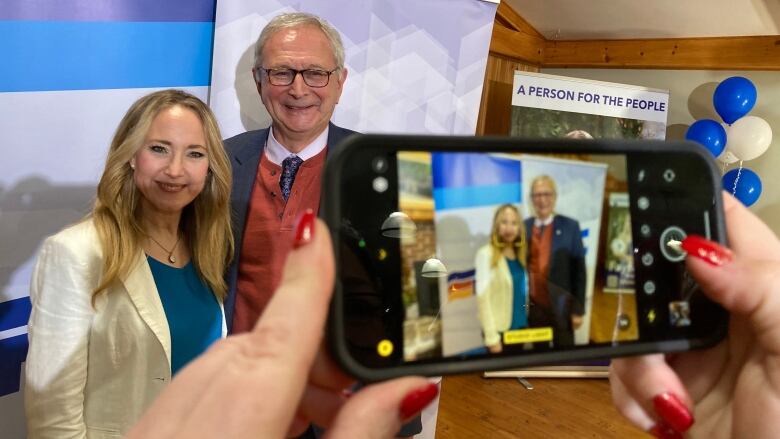 A woman and man pose in a photo together being taken on an IPhone