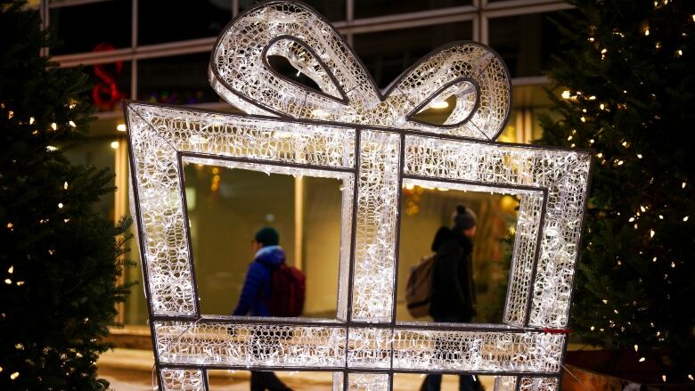 A big lit up display at night looks like a wrapped present. People are walking behind it.