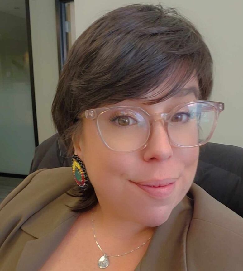 An Indigenous woman in a red shirt and brown blazer