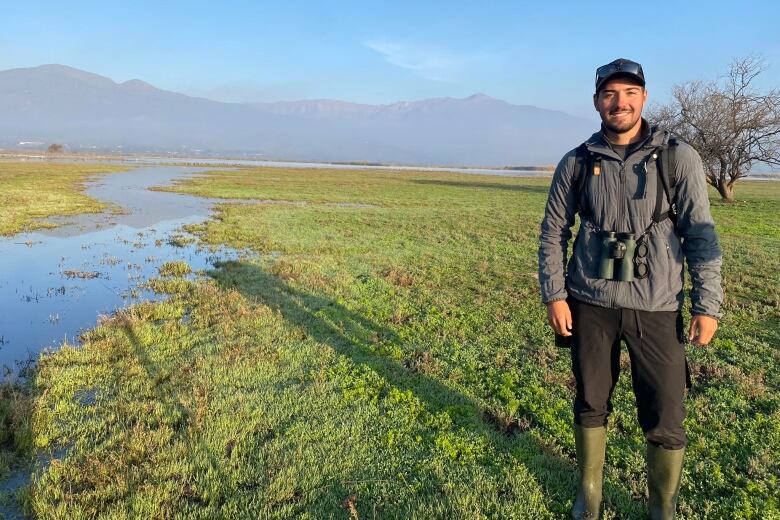 A man stands in a marshy field. 