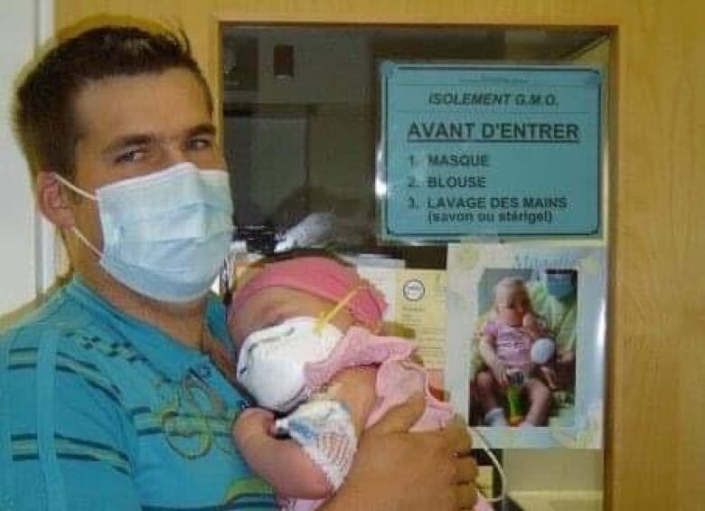 A man wearing a mask holds a baby who is also wearing a mask. he is standing in a hospital. 