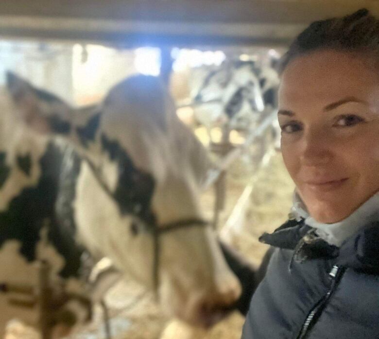 A woman takes a selfie. In the background is a cow. 