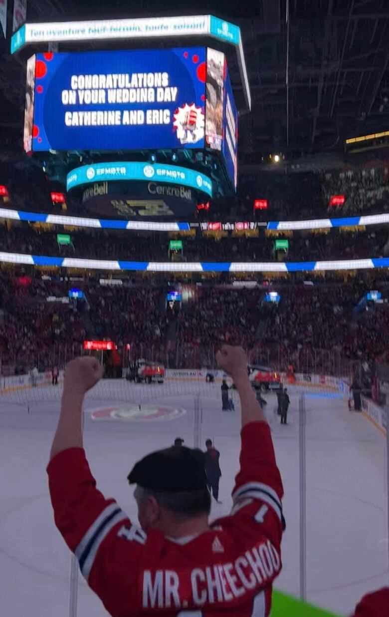 A man raising his hands up a jumbotron screen at a hockey game