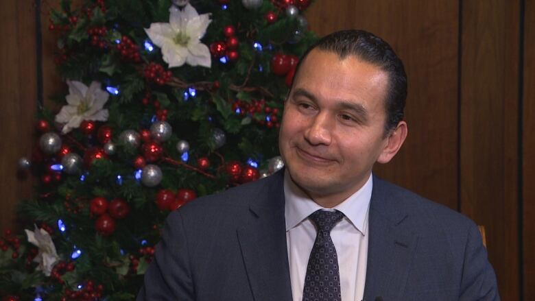 A man sitting next to a Christmas tree.