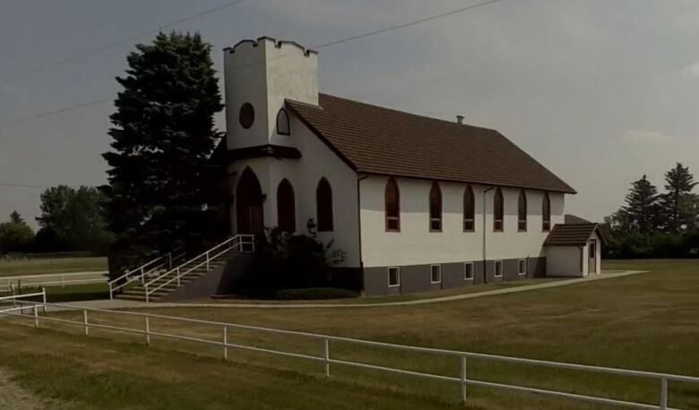 A small white church surrounded by a green lawn out in the country.