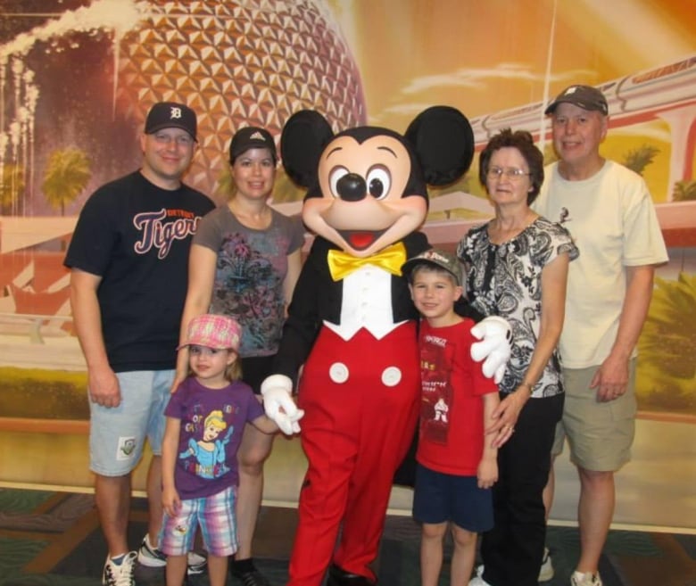 Two adults, two older adults and two young children stand for a photo with Mickey Mouse.