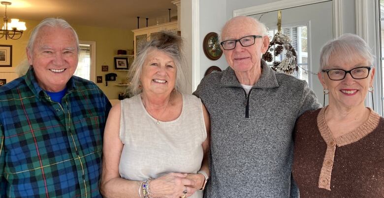 Four smiling people standing side by side and arm in arm.