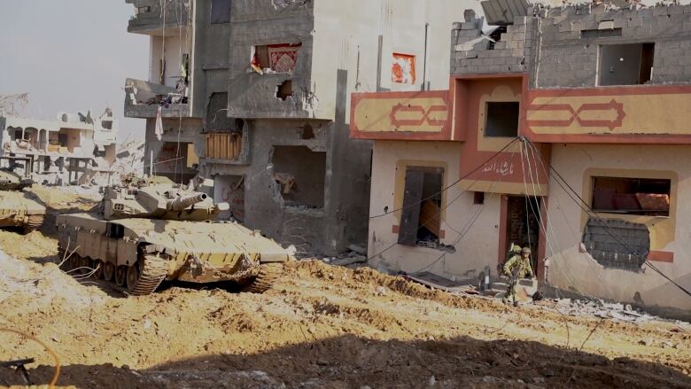 A tank is shown beside a heavily damaged concrete building. 