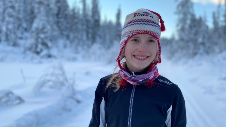 A child standing in a trail during the winter smiles.