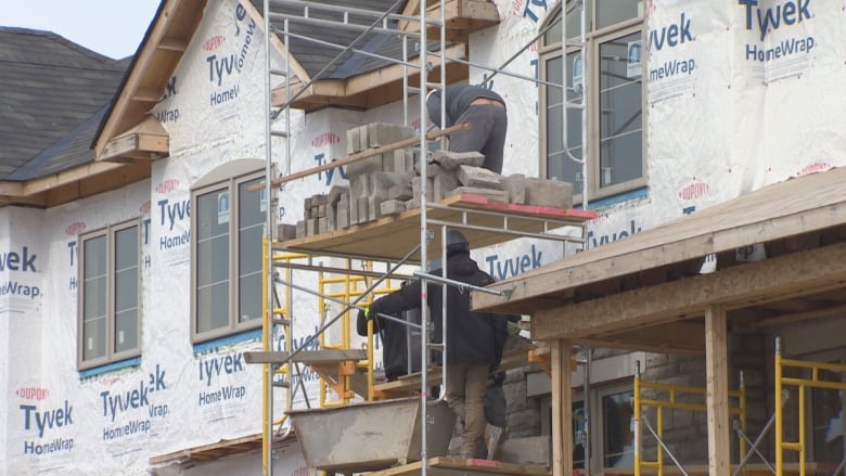 Two workers on scaffolding outside a partial completed new home. 