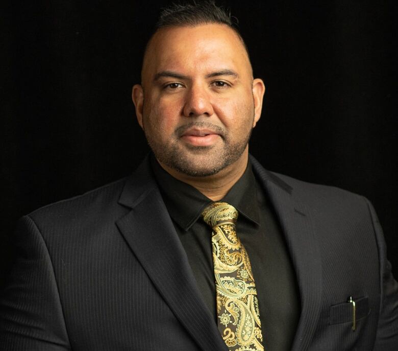 A man in a suit smiles for the camera in a headshot with a black background