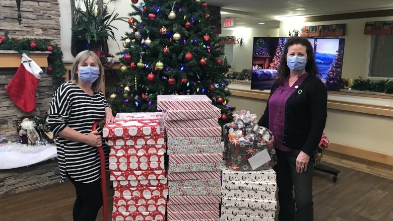 Two women stand next to a cart containing piles of gift boxes.