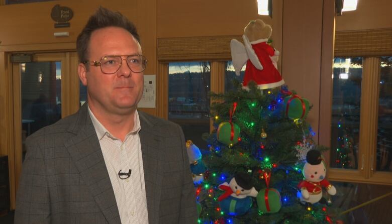 A man talks to a reporter with a Christmas tree in the background.