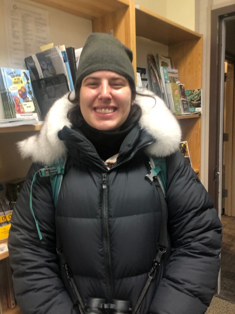 Woman wearing a winter jacket, with binoculars around her neck, smiles for a picture