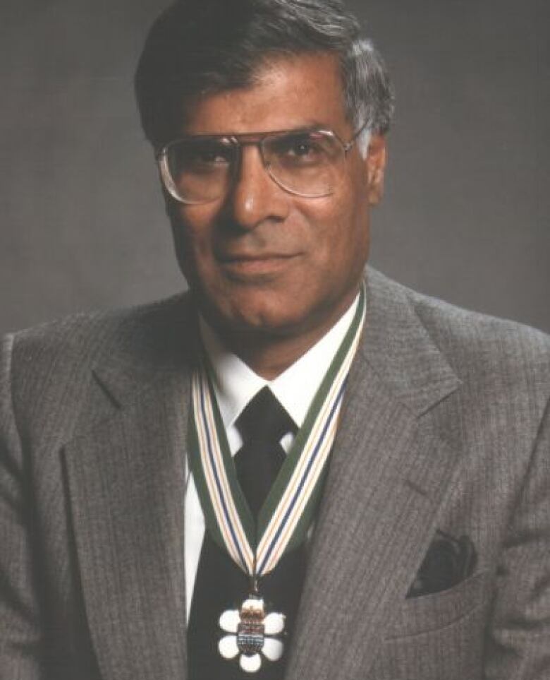 A man smiles slightly in a suit as he wears a medal around his neck.