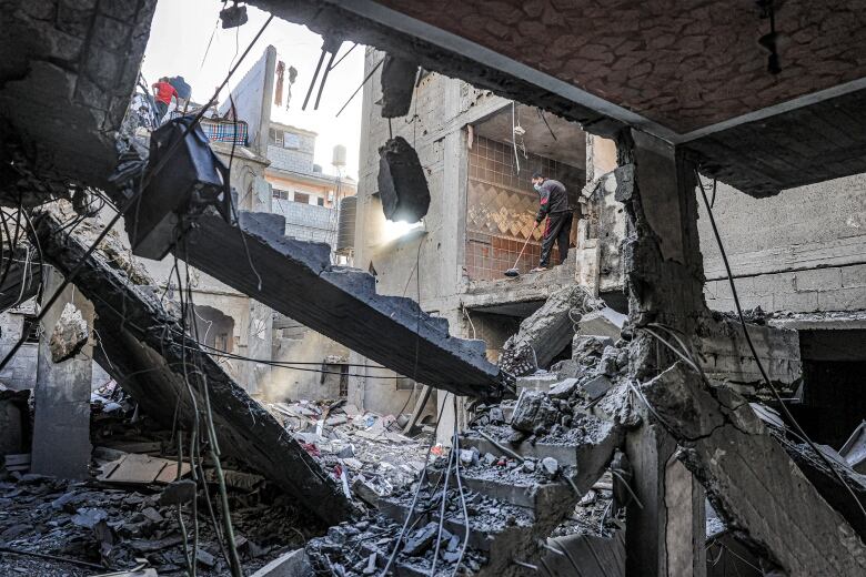 A man sweeps a room with an empty wall overlooking a building destroyed by Israeli bombardment in Rafah in the southern Gaza Strip.