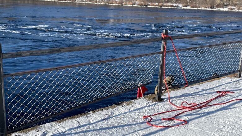 A fence dividing the riverbank from the water. The lower part of the fence is damaged forming a hole. 