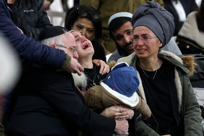 A woman throws her head back in anguish as others look on in concern.