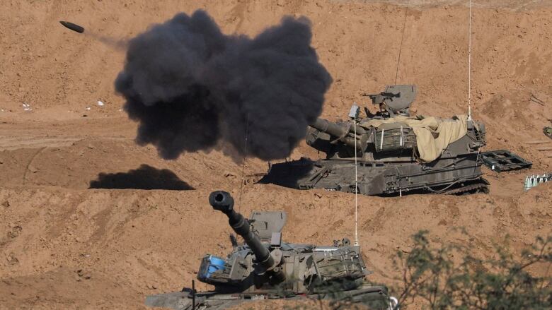 Two tanks in a barren landscape. A projectile is visible leaving the barrel of one, leaving behind a cloud of dark smoke.