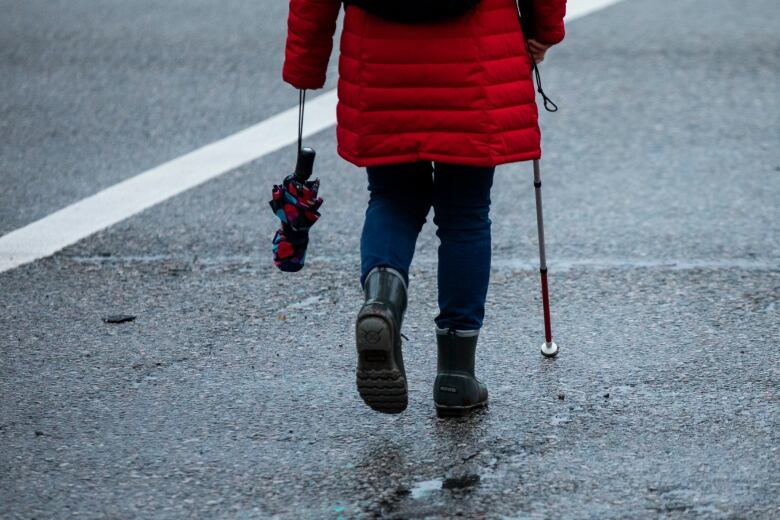 Someone walks down a street using a blind cane. 