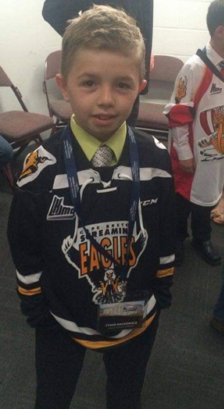 A young boy is shown in a a Cape Breton Screaming Eagles jersey inside a hockey locker room.