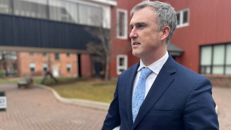 A man with a blue suit and tie stands in front of a courthouse in Charlottetown, Prince Edward Island.