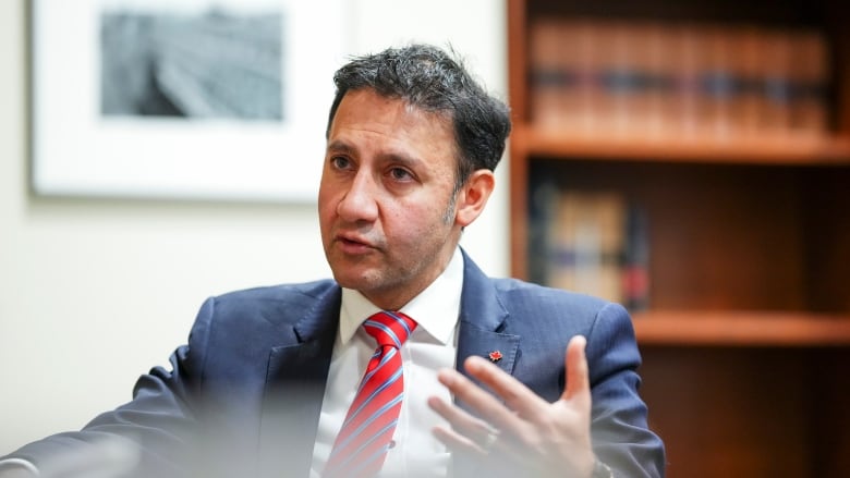 A man in a suit sitting in front of a bookshelf.