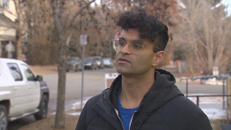 A man with glasses and a black jacket outdoors on a cloudy day