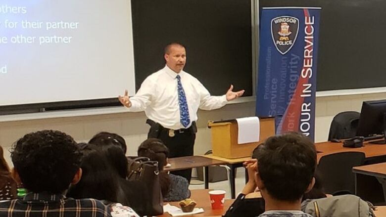 A police officer in a suit speaks to college students.