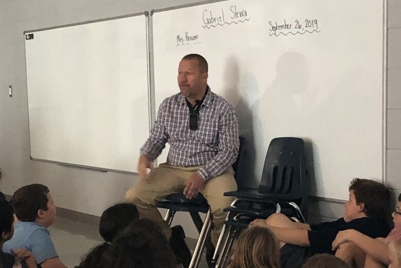 A man sits in a classroom addressing students.