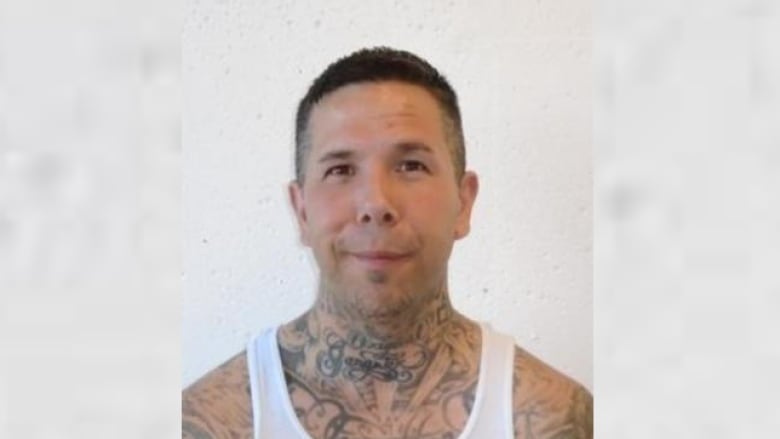 A man with tattoos on his neck and shoulders is pictured wearing a white sleeveless shirt.