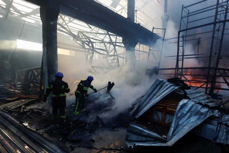 Two helmeted people work amid smoke and twisted metal.