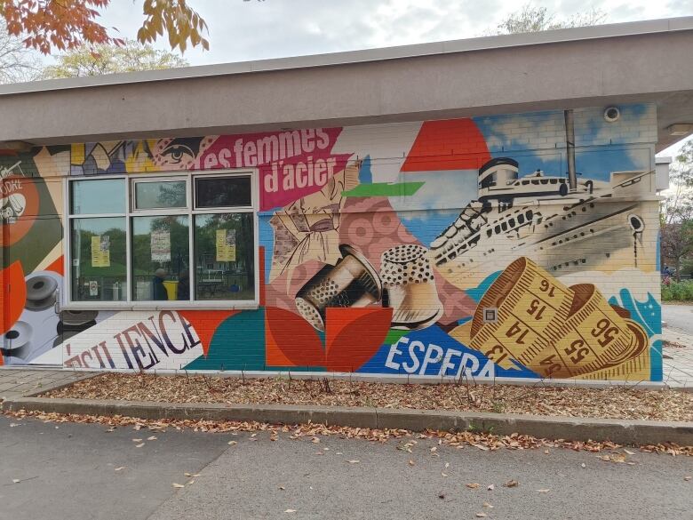 A mural on the side of a building depicting a ship, measuring ribbon a thumb guard and bobbins and text that says 