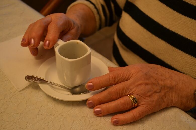 A woman's elderly hands holding a cup of espresso. 