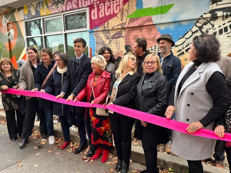 A group of people standing behind a pink ribbon during a mural inauguration. 